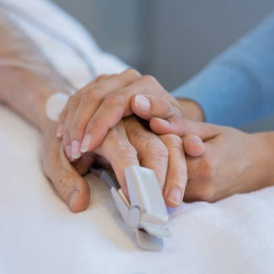 Daughter holding the hand of an elderly father. Closeup of woman holding senior man hand in hospital. Close up of nurse holding old man hand with oxygen saturated probe on finger.